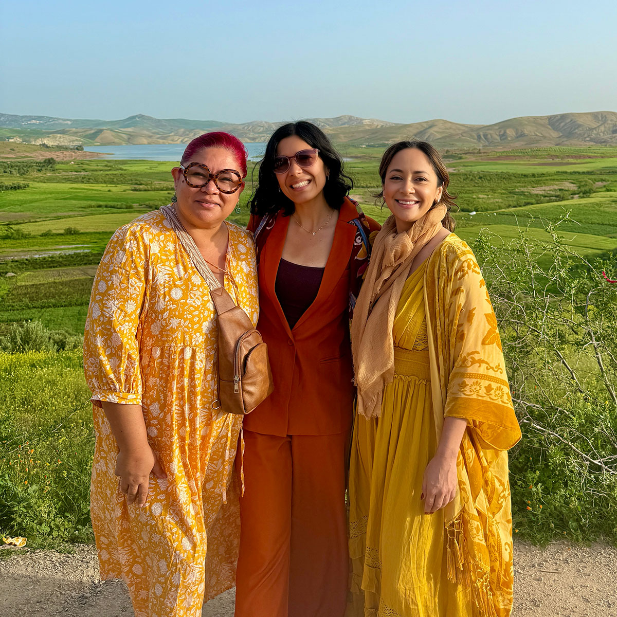 photo of three women standing in front of green hills