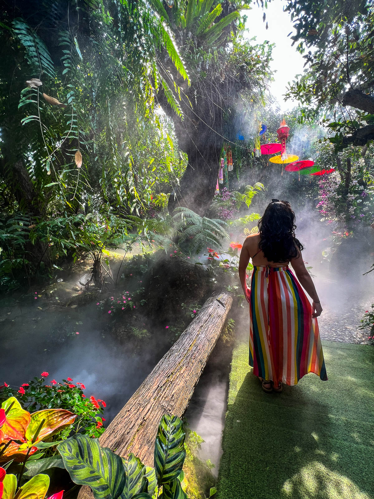 A traveler in a striped dress walking a misty garden path in Thailand