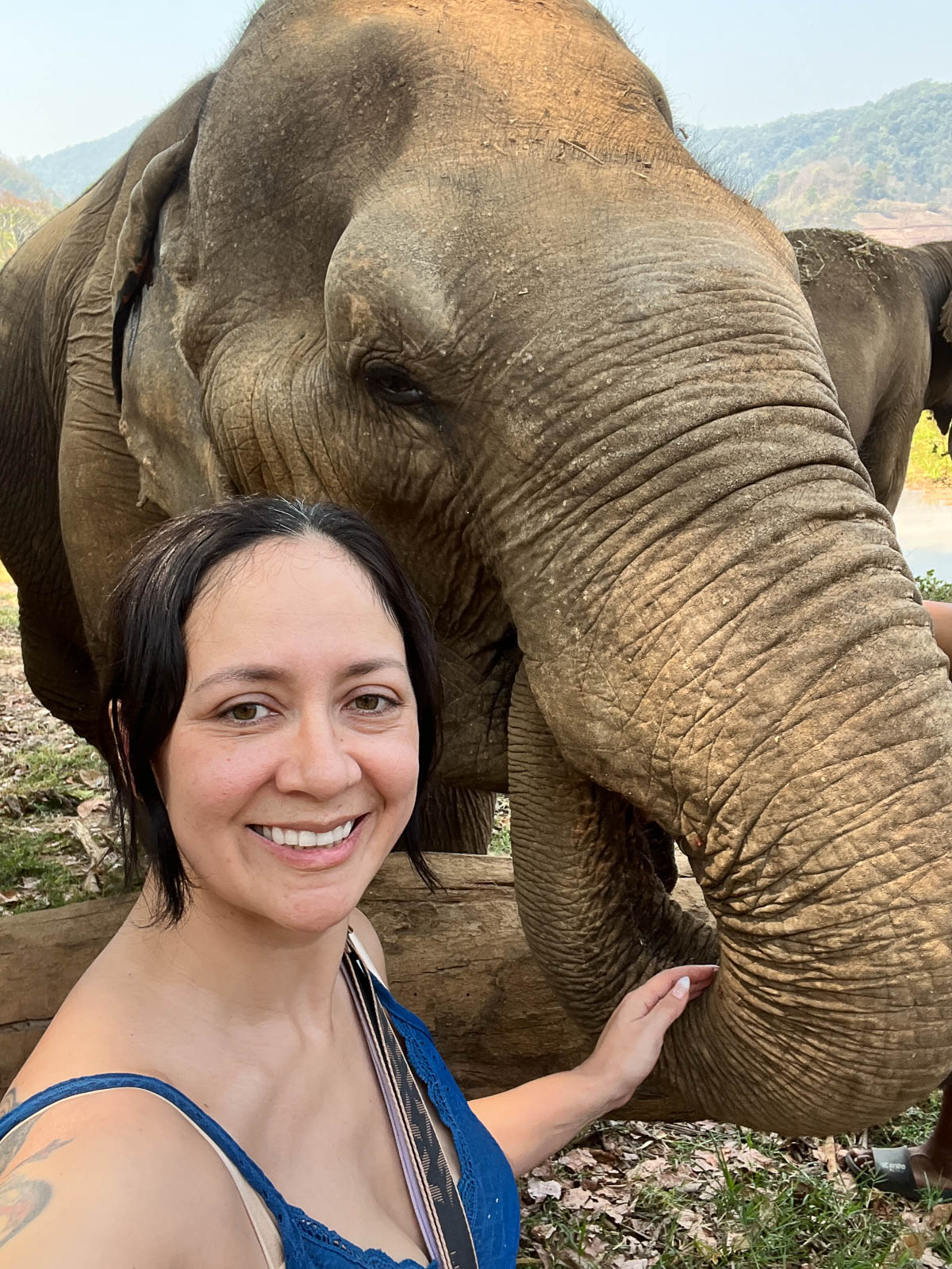 A traveler smiling beside an elephant at a sanctuary in Thailand