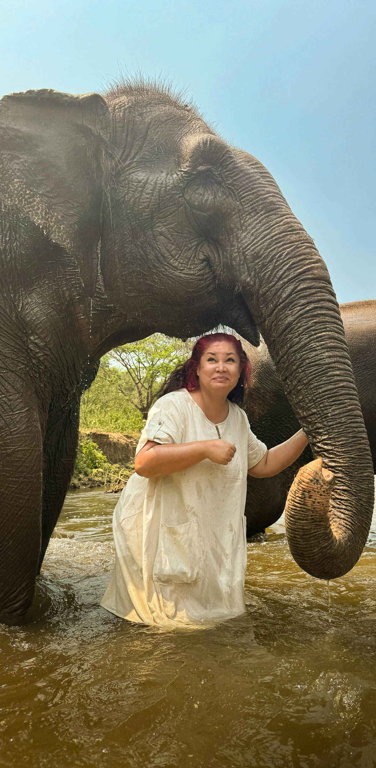 A traveler in a white dress standing with an elephant in Thailand