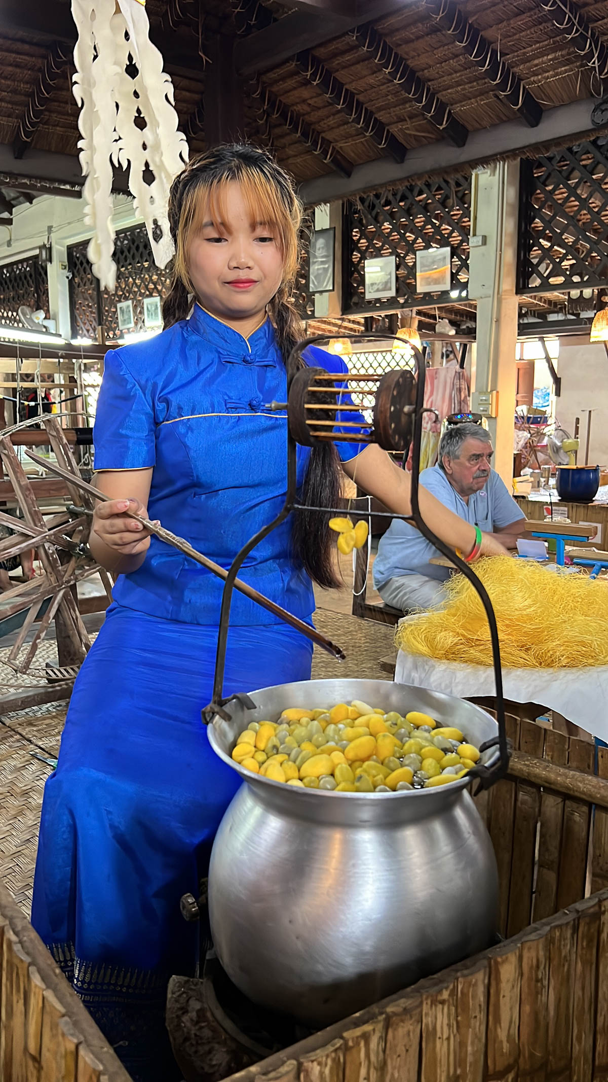 A cook in a blue shirt stirring a large pot at a market in Thailand