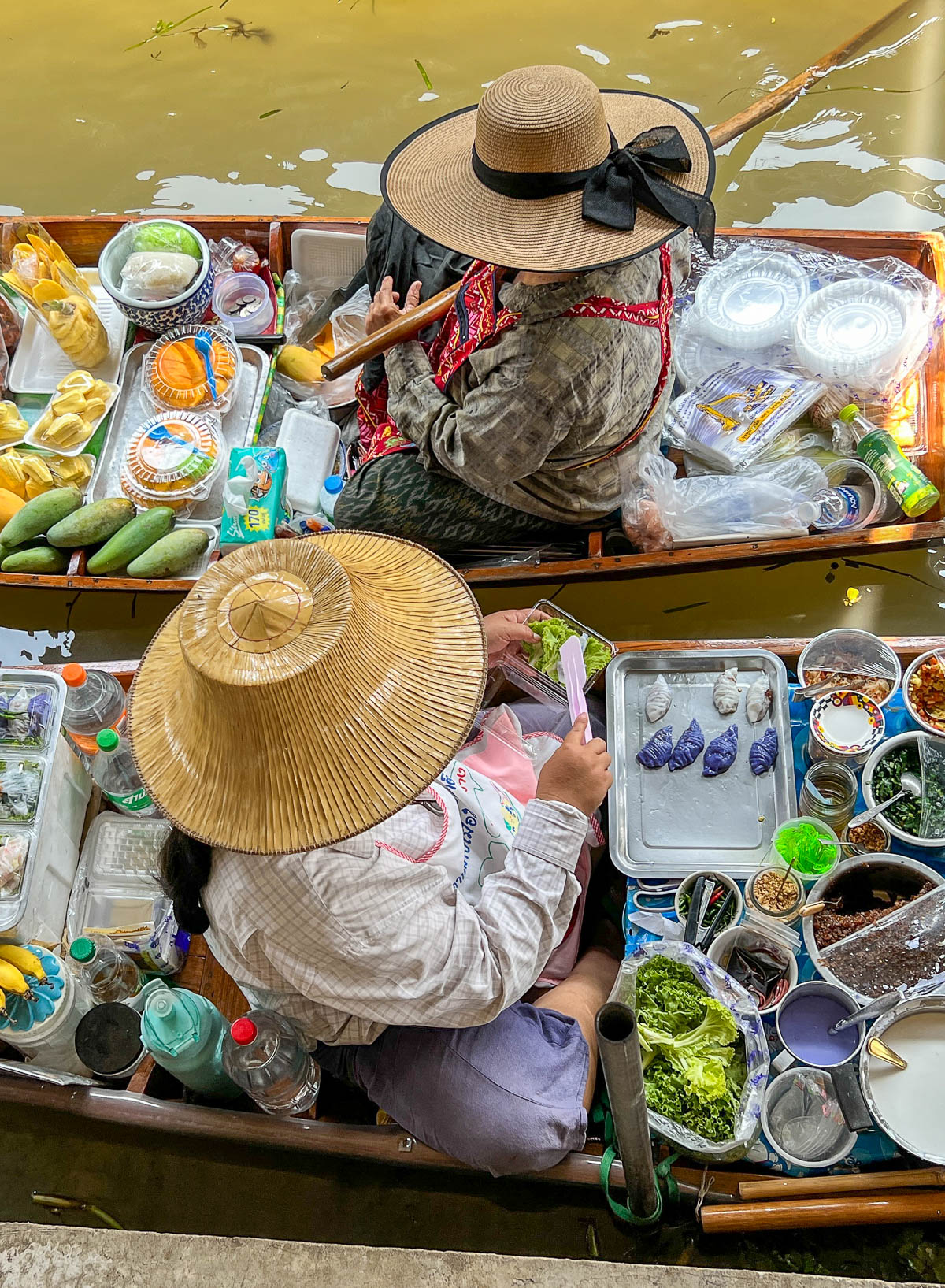 A vendor in a straw hat selling produce from a boat at a floating market in Thailand