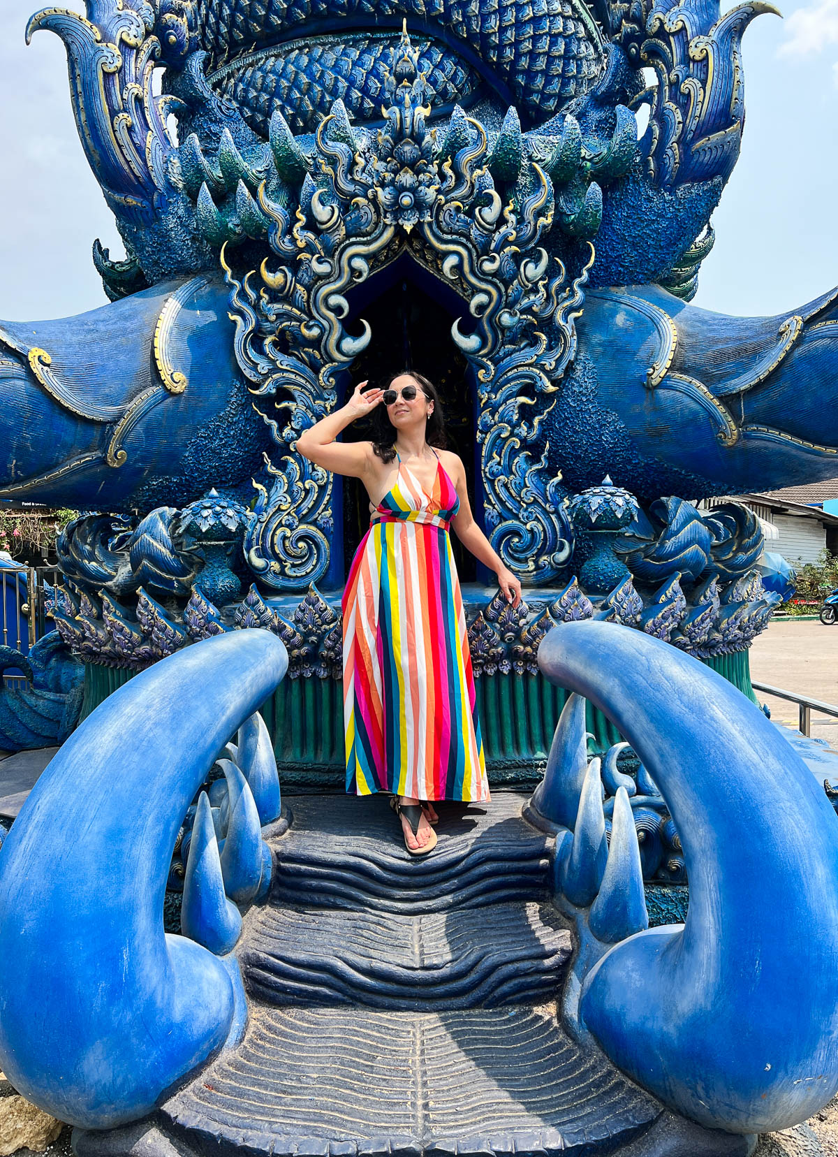 A traveler in a striped dress posing among blue sculptures at a temple in Thailand
