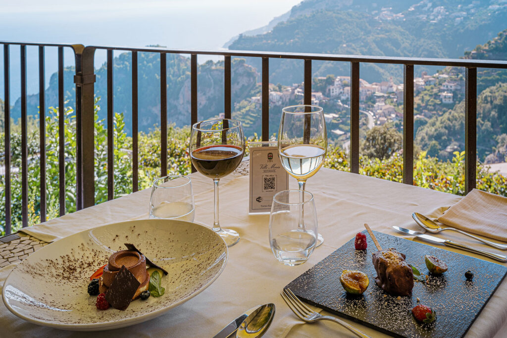 A table set with wine and gourmet food with a hillside view at the Villa Maria restaurant in Ravello.