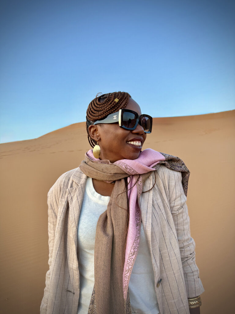 Fashionable woman with sunglasses smiling and standing in the sand dunes.