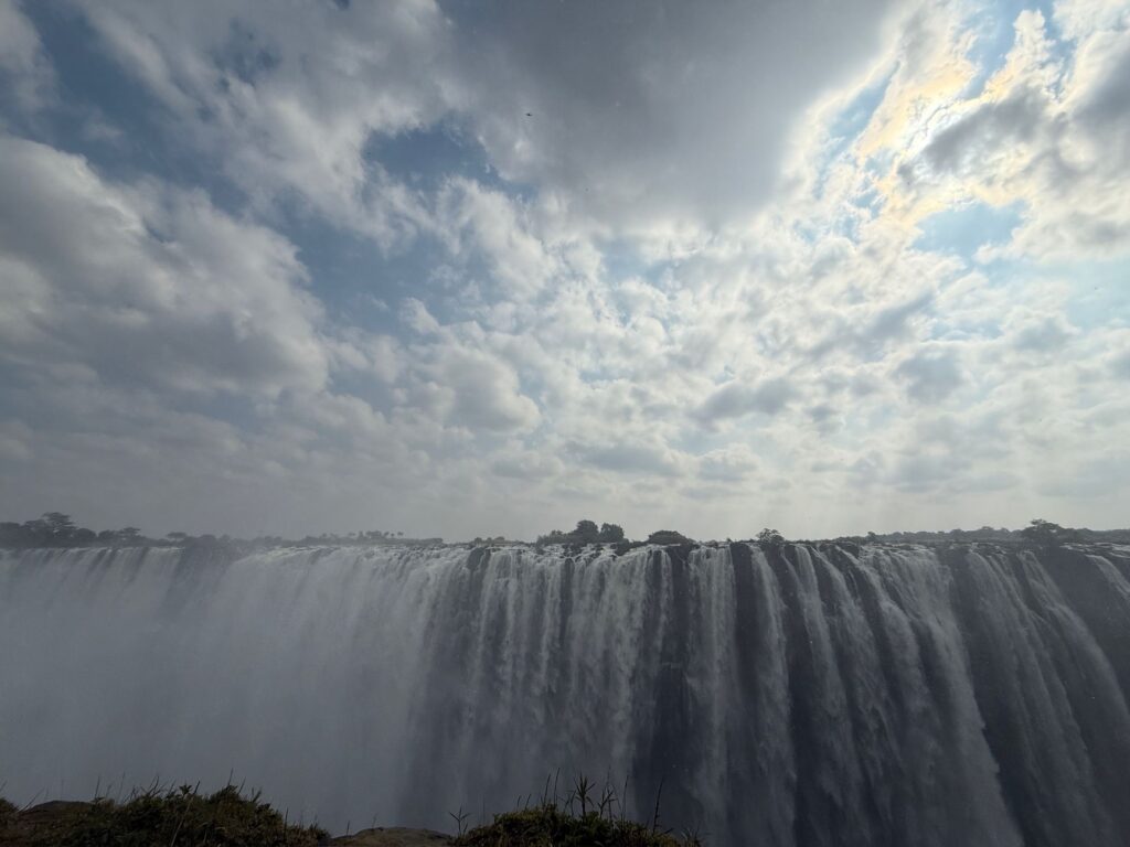 Wide view of Victoria Falls pouring over the cliff under a dramatic cloudy sky