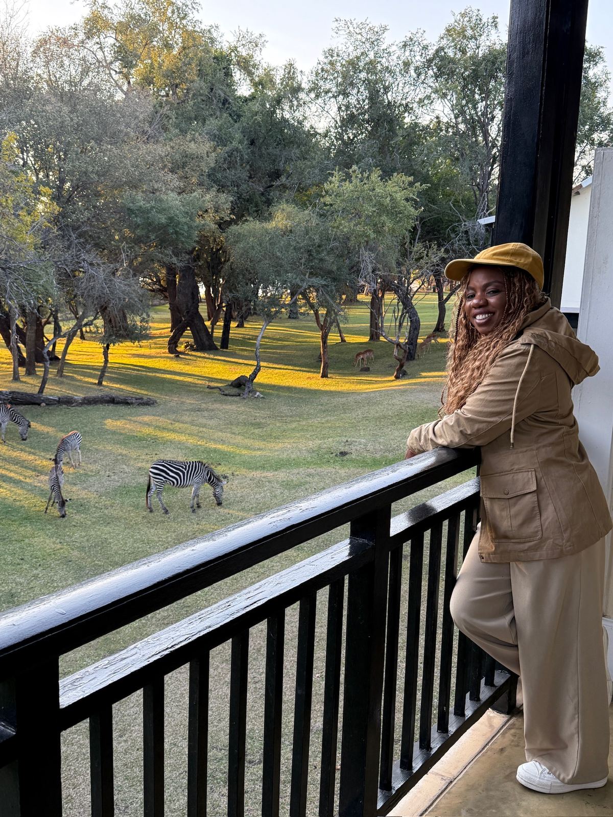 A woman on a balcony at The Royal Livingstone watching zebras and impala graze at golden hour