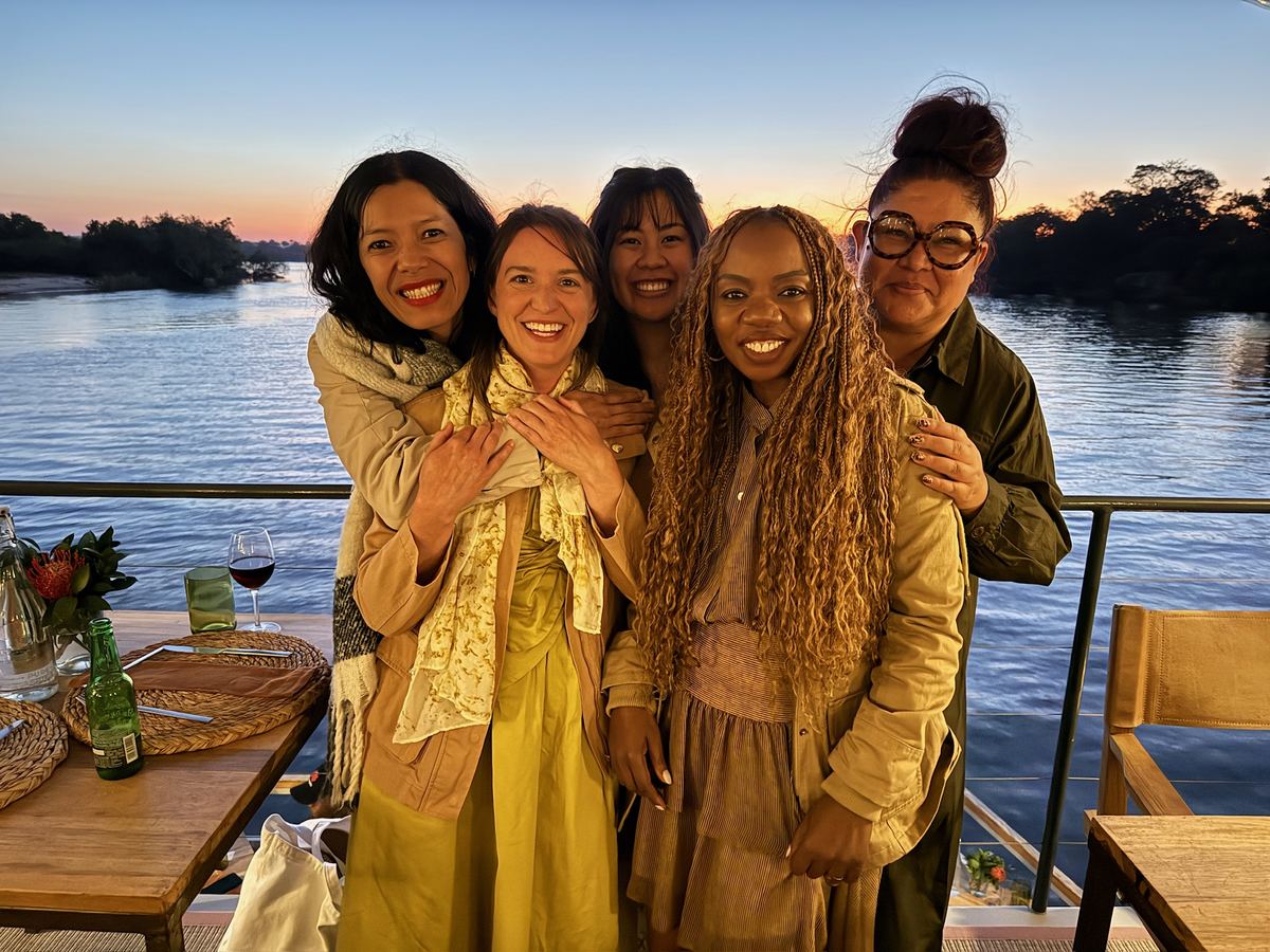 Five women hugging on the deck of a Zambezi River dinner cruise at sunset