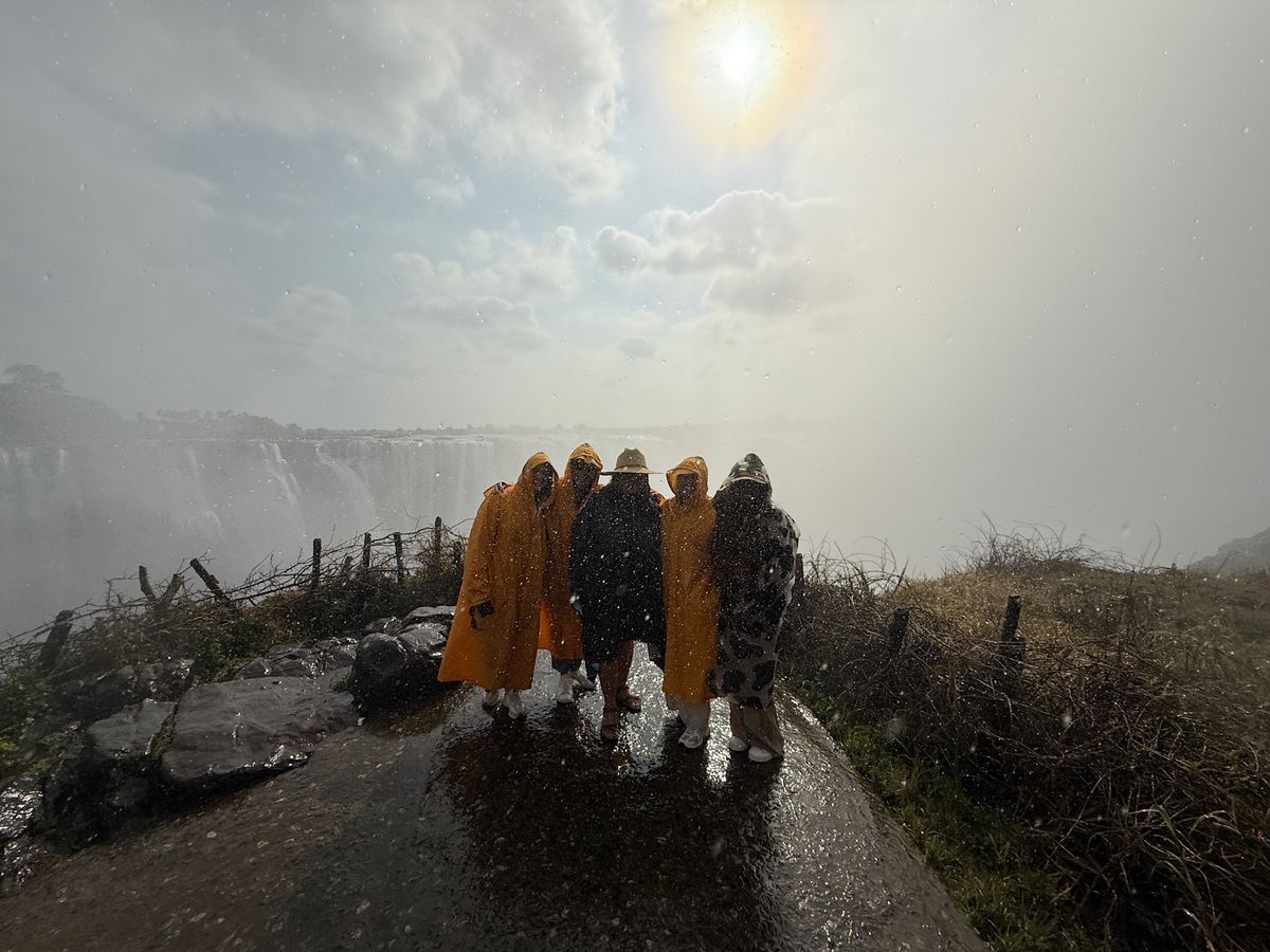 Five women in ponchos silhouetted on a wet viewpoint in the mist of Victoria Falls