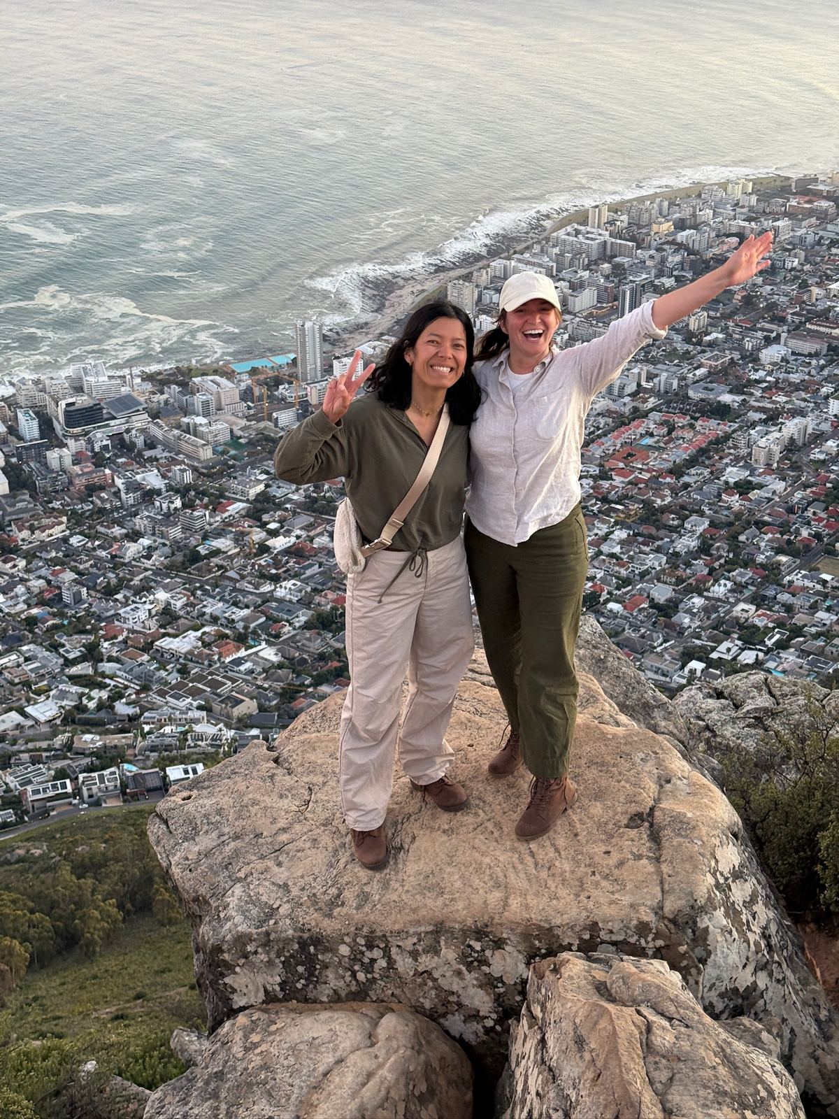 Two women with arms outstretched on a rock at the top of Lion's Head above the city
