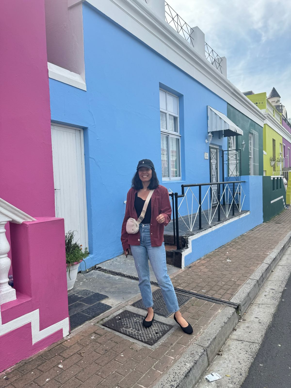 A woman on the sidewalk beside pink, blue, and green houses in Bo-Kaap