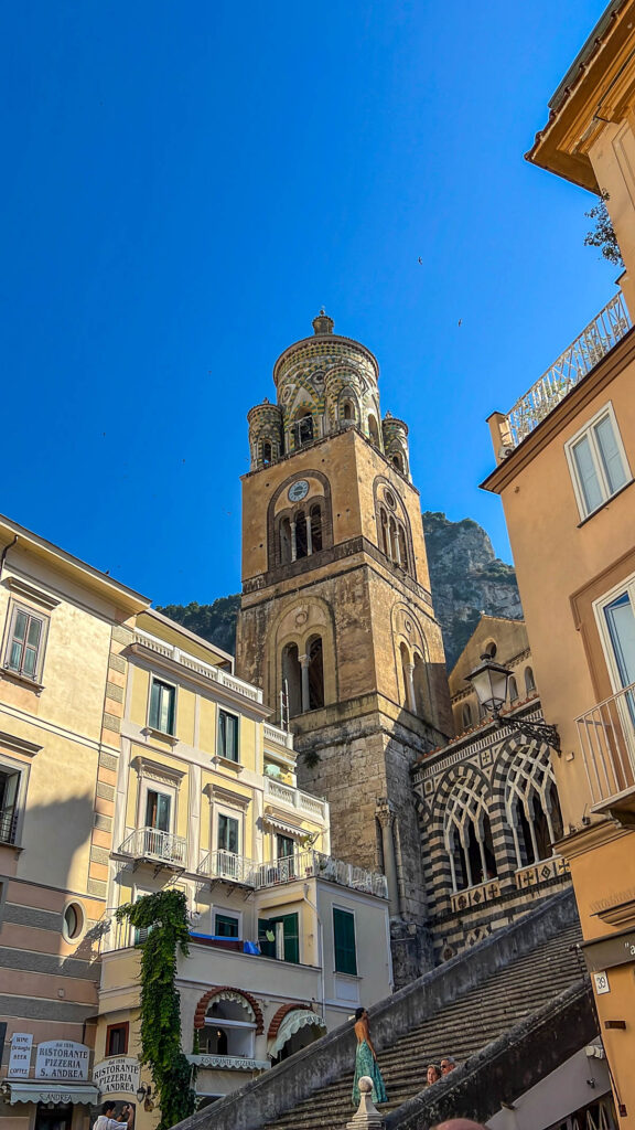The striped bell tower of Amalfi Cathedral against a blue sky.