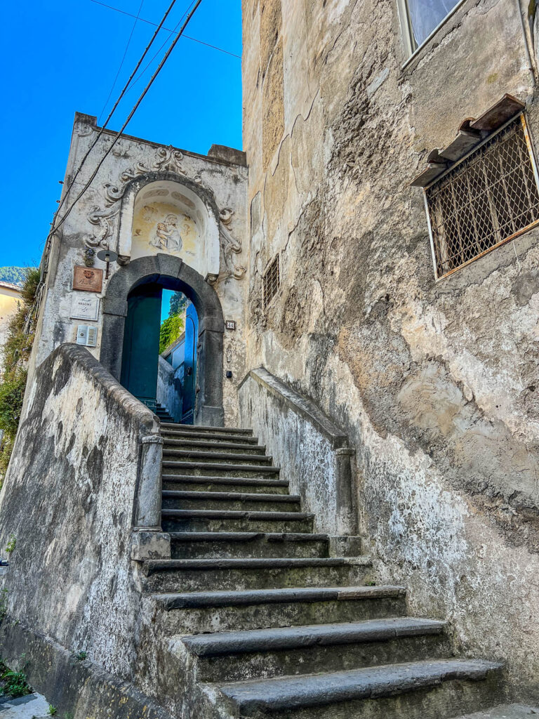 A worn stone staircase leading up to an arched doorway in Amalfi.