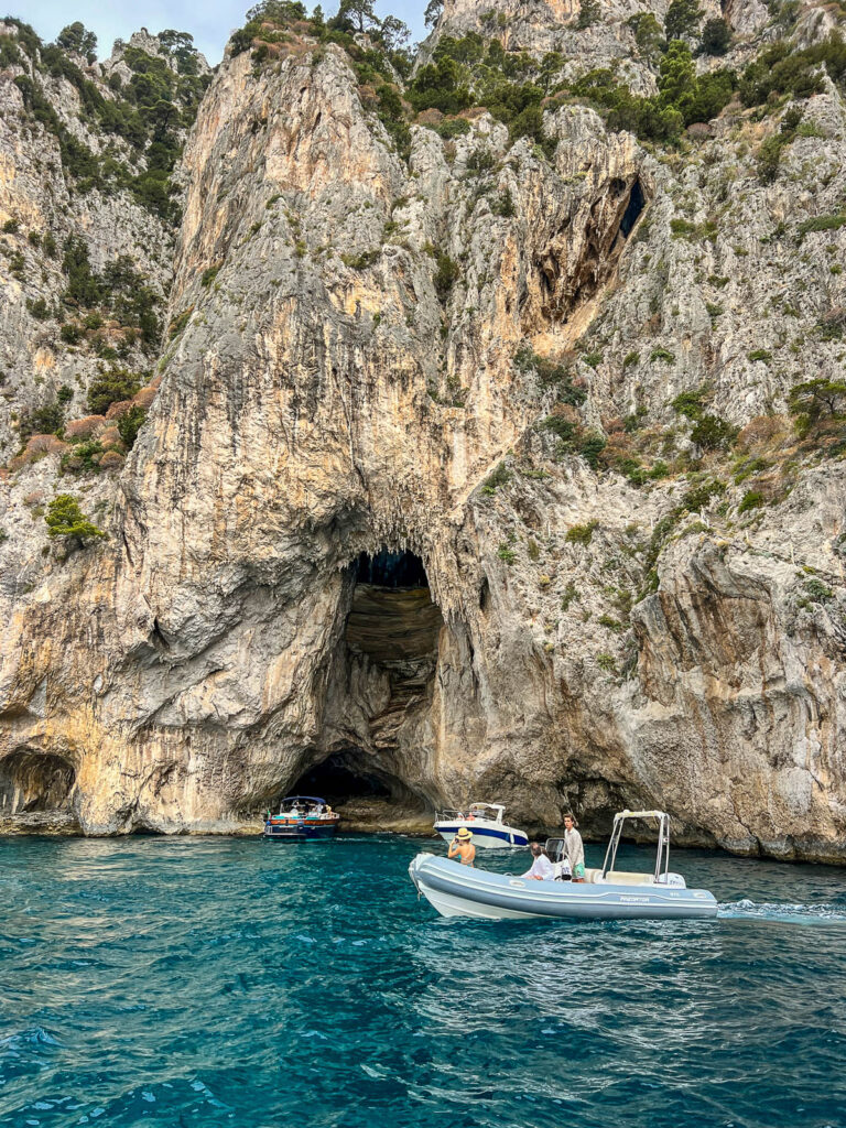 A small boat beside a sea cave in pale limestone cliffs near Capri.