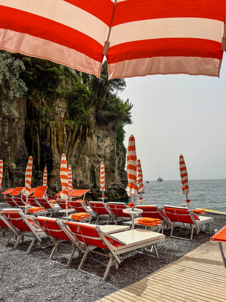 Orange and white striped umbrellas and sunbeds beside the cliff at Arienzo Beach Club.