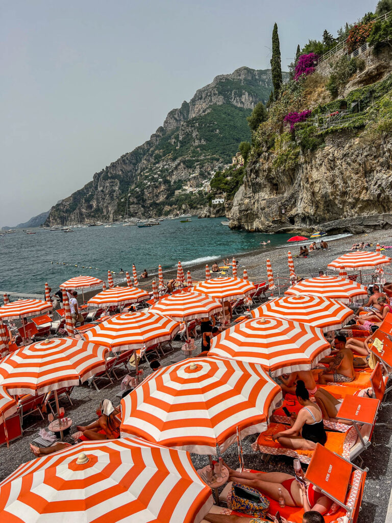 Rows of orange and white striped umbrellas at Arienzo Beach Club in Positano, seen from above.