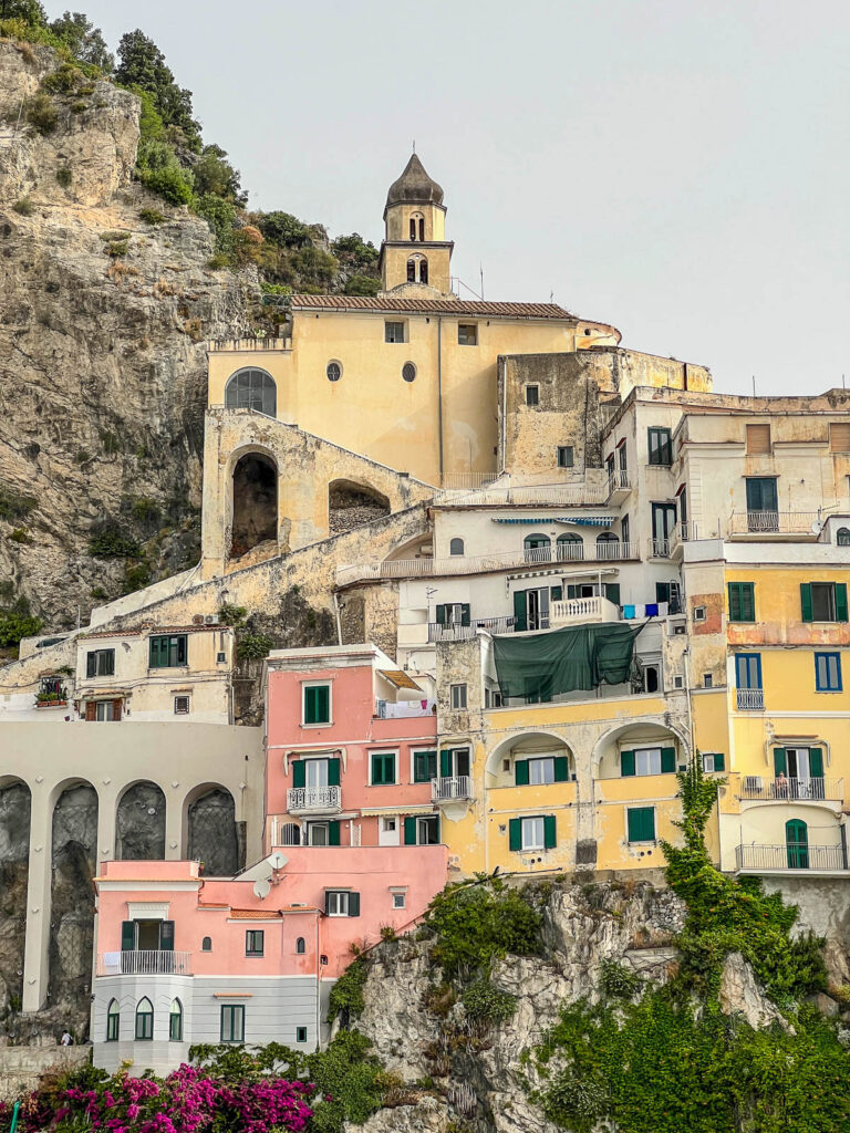 Pastel buildings and a clifftop church above the harbor in Amalfi.