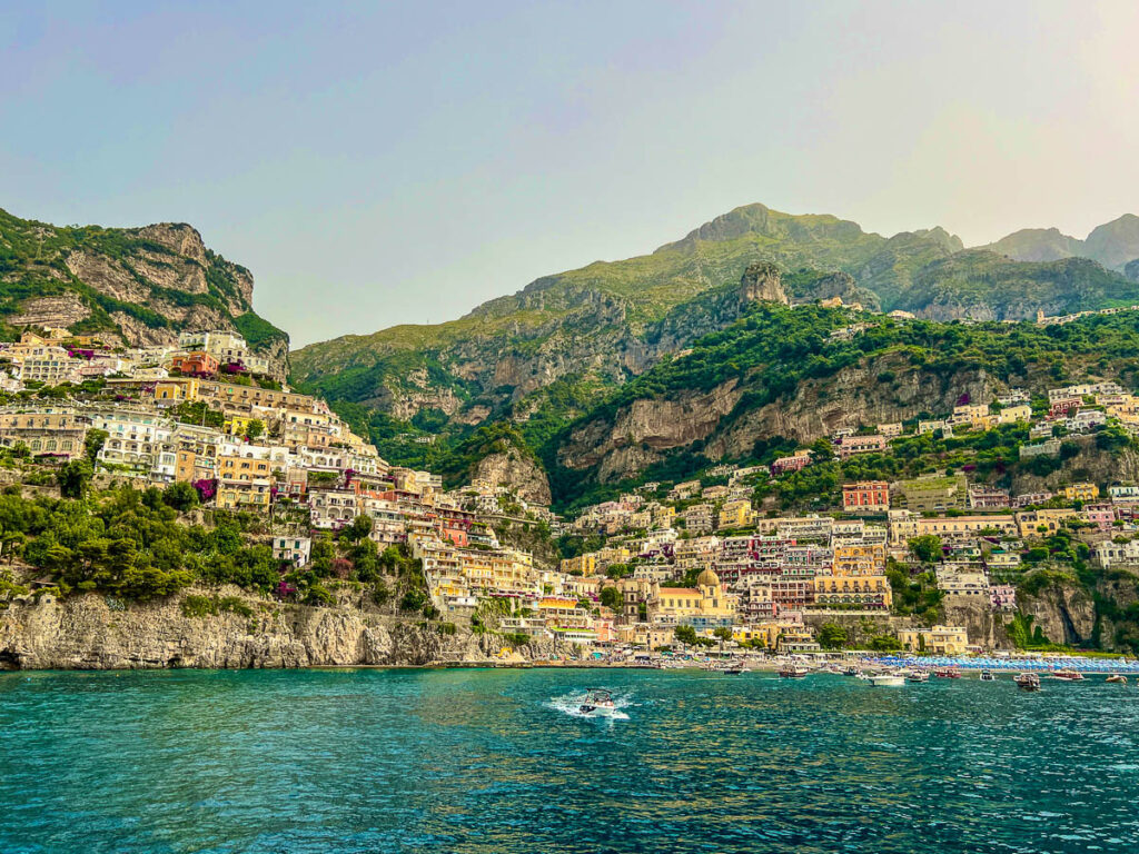 Positano seen from the water, with pastel buildings climbing the hillside above turquoise sea.