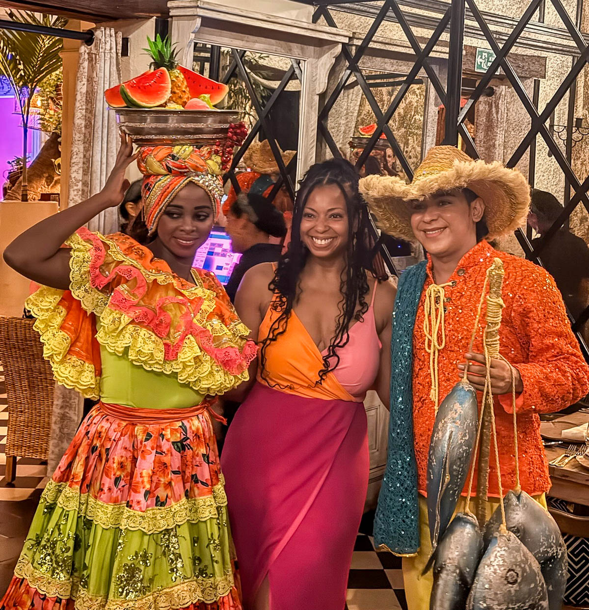 Woman posing with two costumed performers, one balancing a bowl of fruit on her head, at Candé in Cartagena
