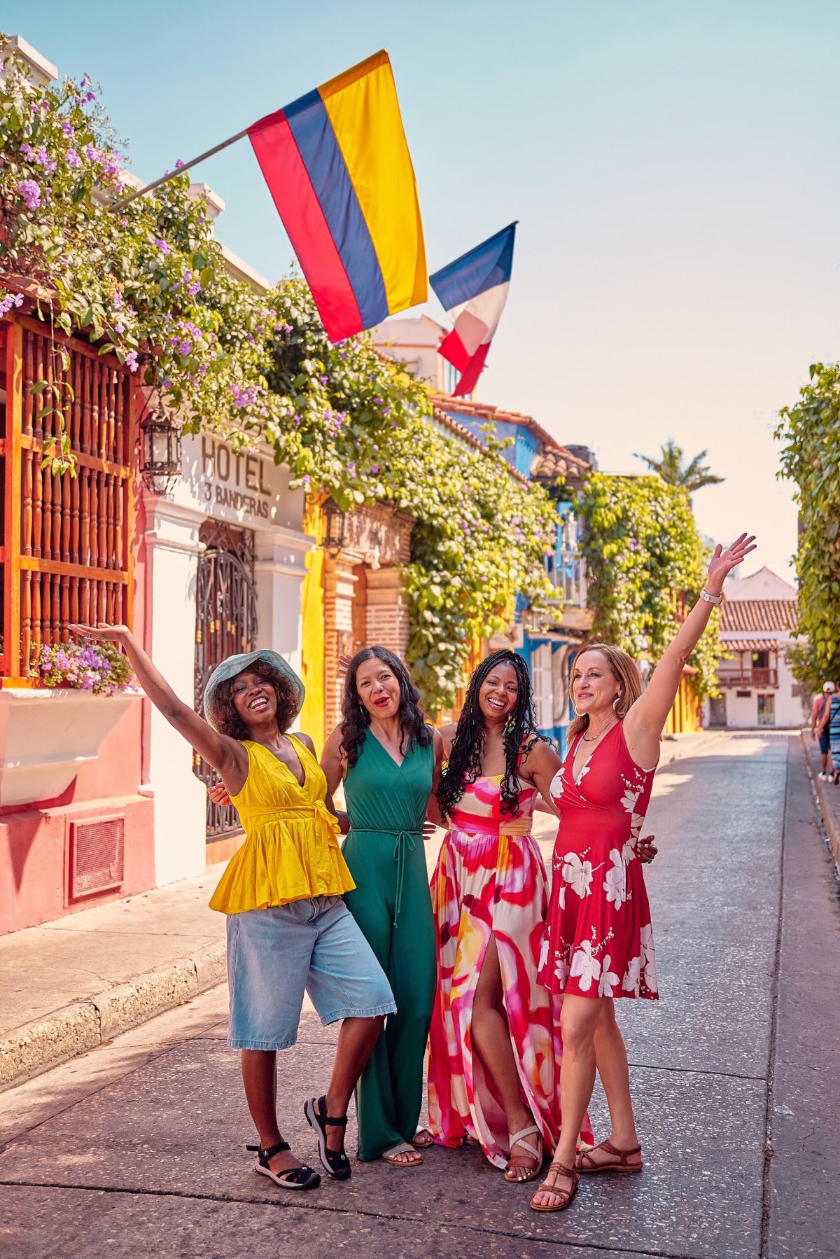 Four friends cheering on a Cartagena street under a Colombian flag and bougainvillea