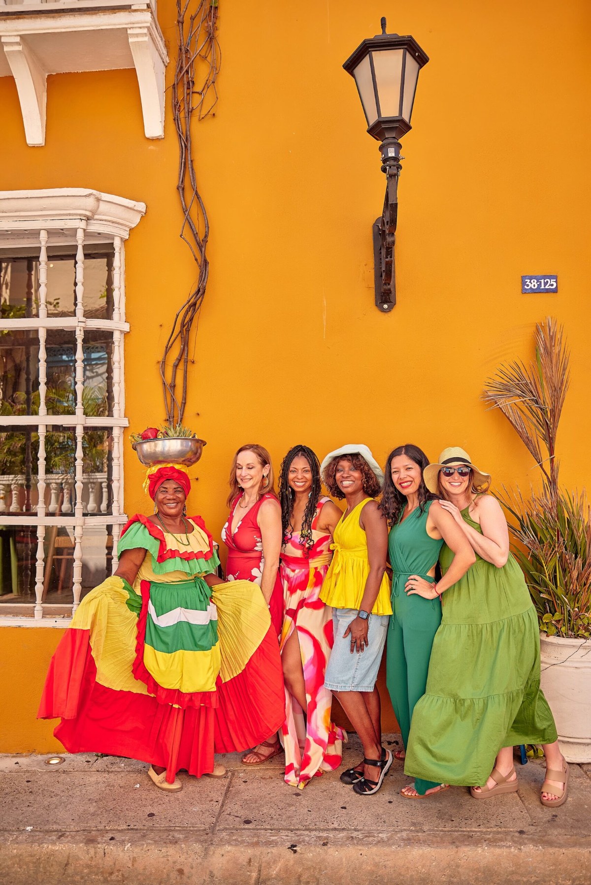 Our group posing with a palenquera in a red, yellow, and green dress against a bright yellow wall in Cartagena
