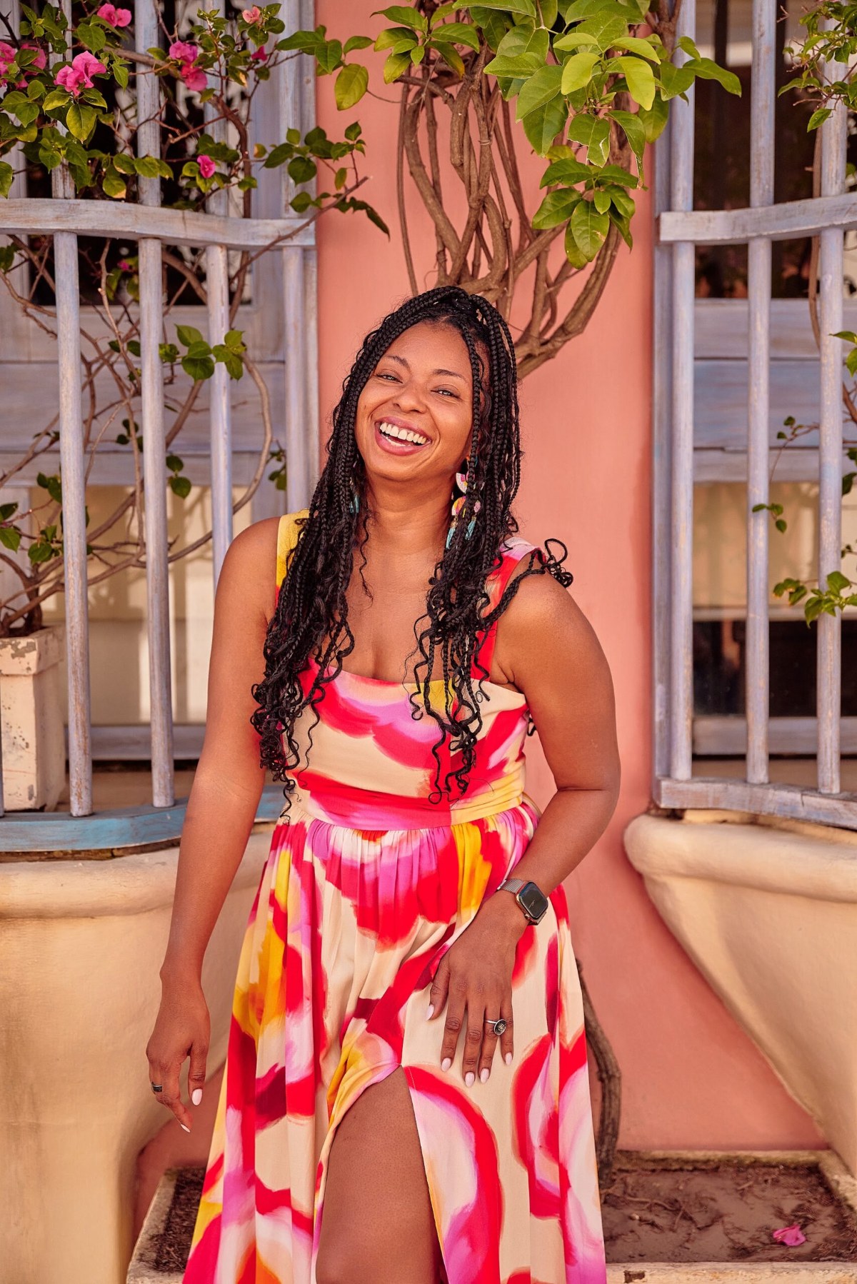 Woman in a pink and yellow dress laughing in front of a window with iron bars and bougainvillea in Cartagena