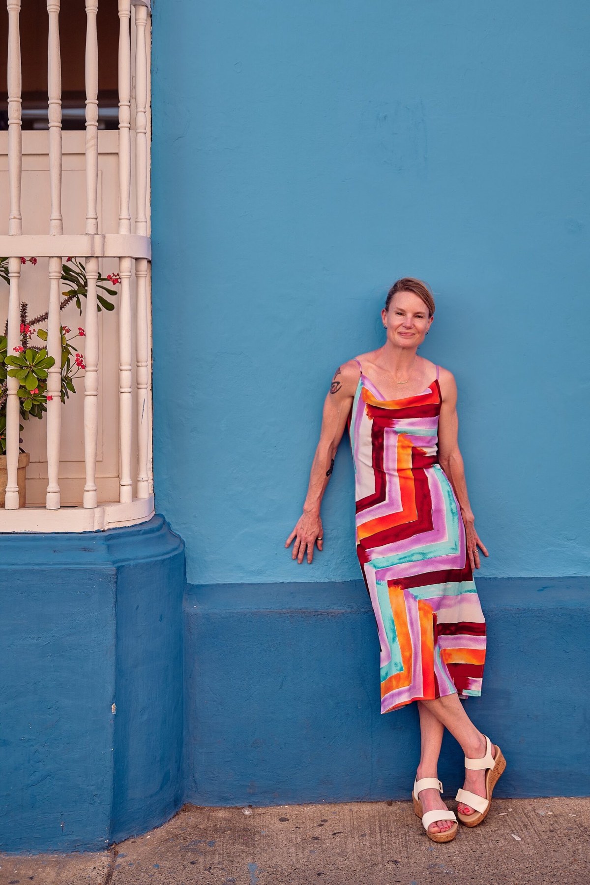 Woman in a striped dress leaning against a bright blue wall in Cartagena