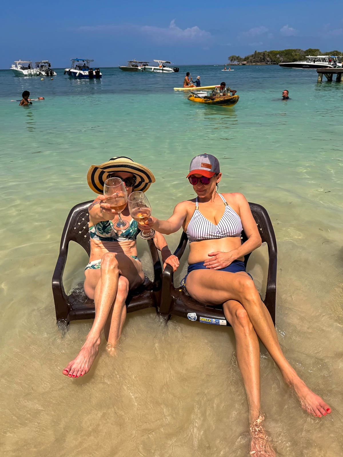 Two friends sitting in chairs set in shallow turquoise water in the Rosario Islands