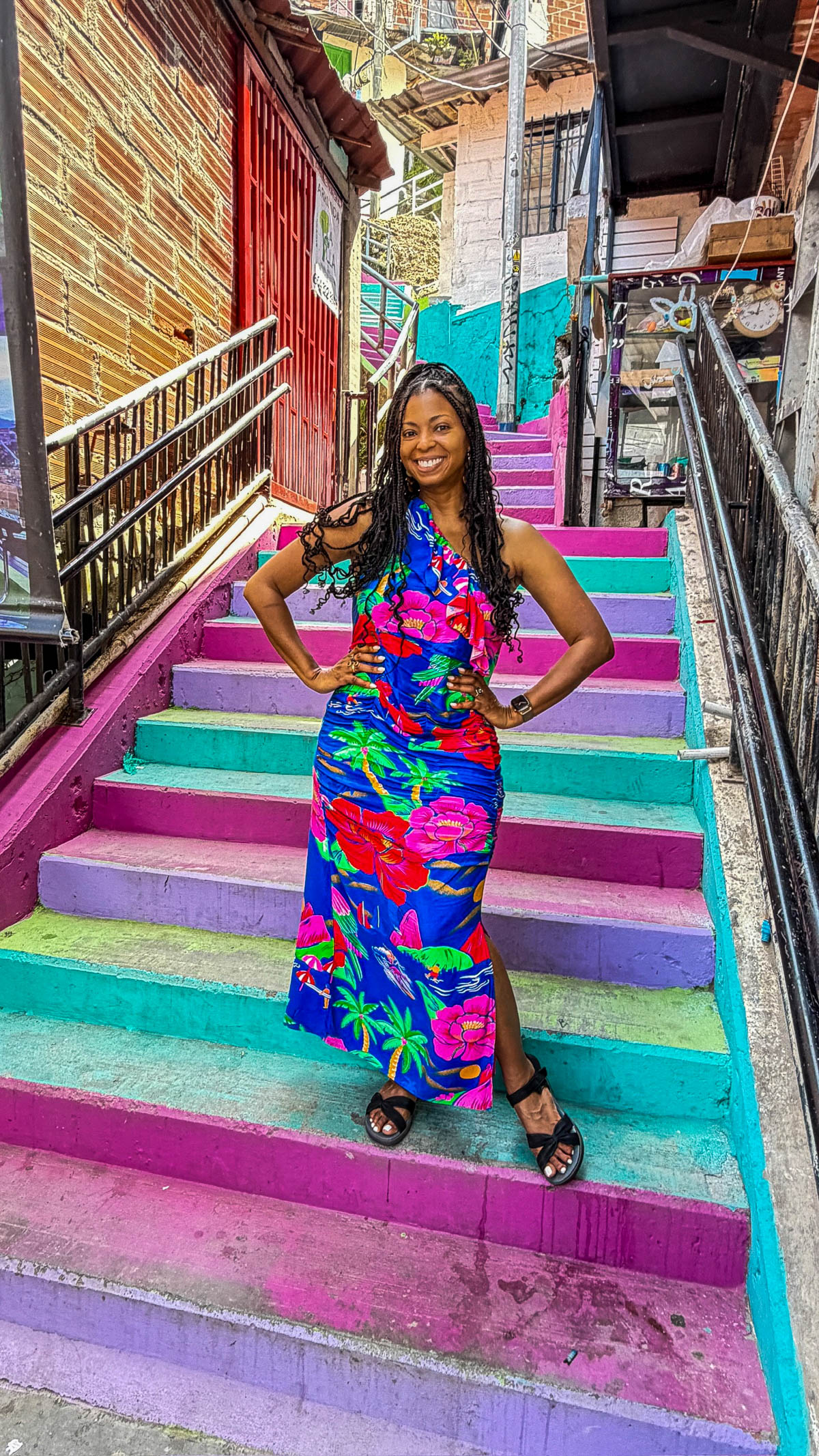 Woman in a bright floral dress standing on rainbow painted stairs in Comuna 13