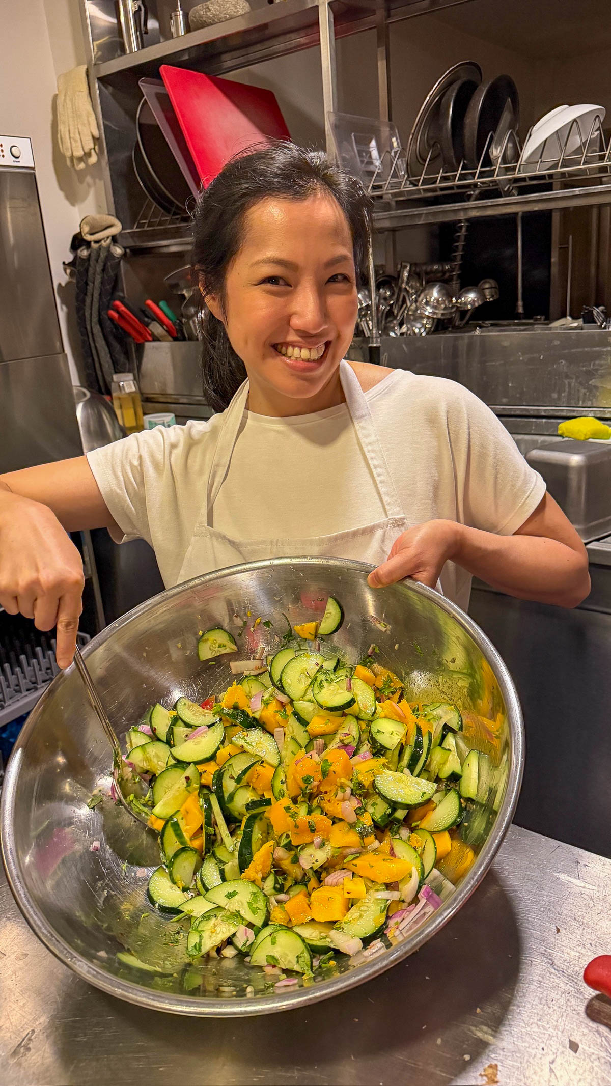 Woman holding a large bowl of cucumber and mango salad at our cooking class