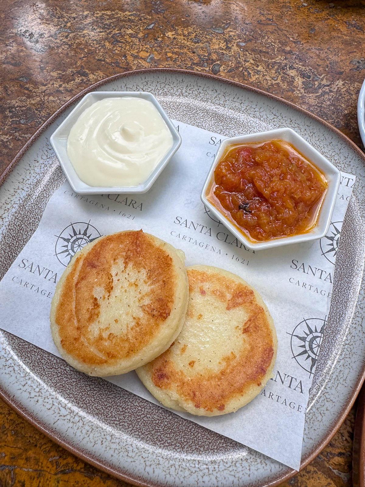 Two arepas served with cream and a red sauce