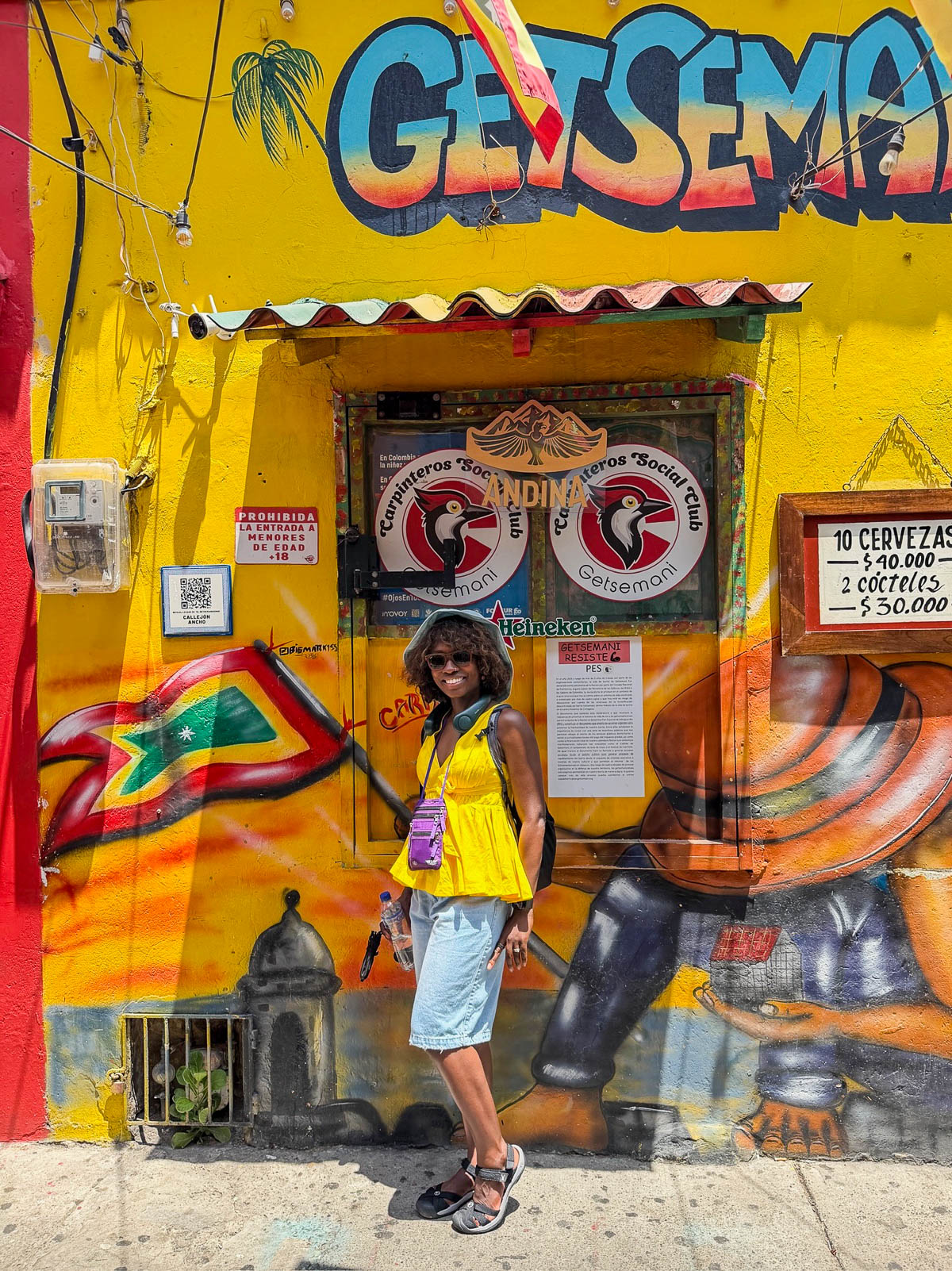 Traveler posing in front of the bright yellow Getsemaní mural
