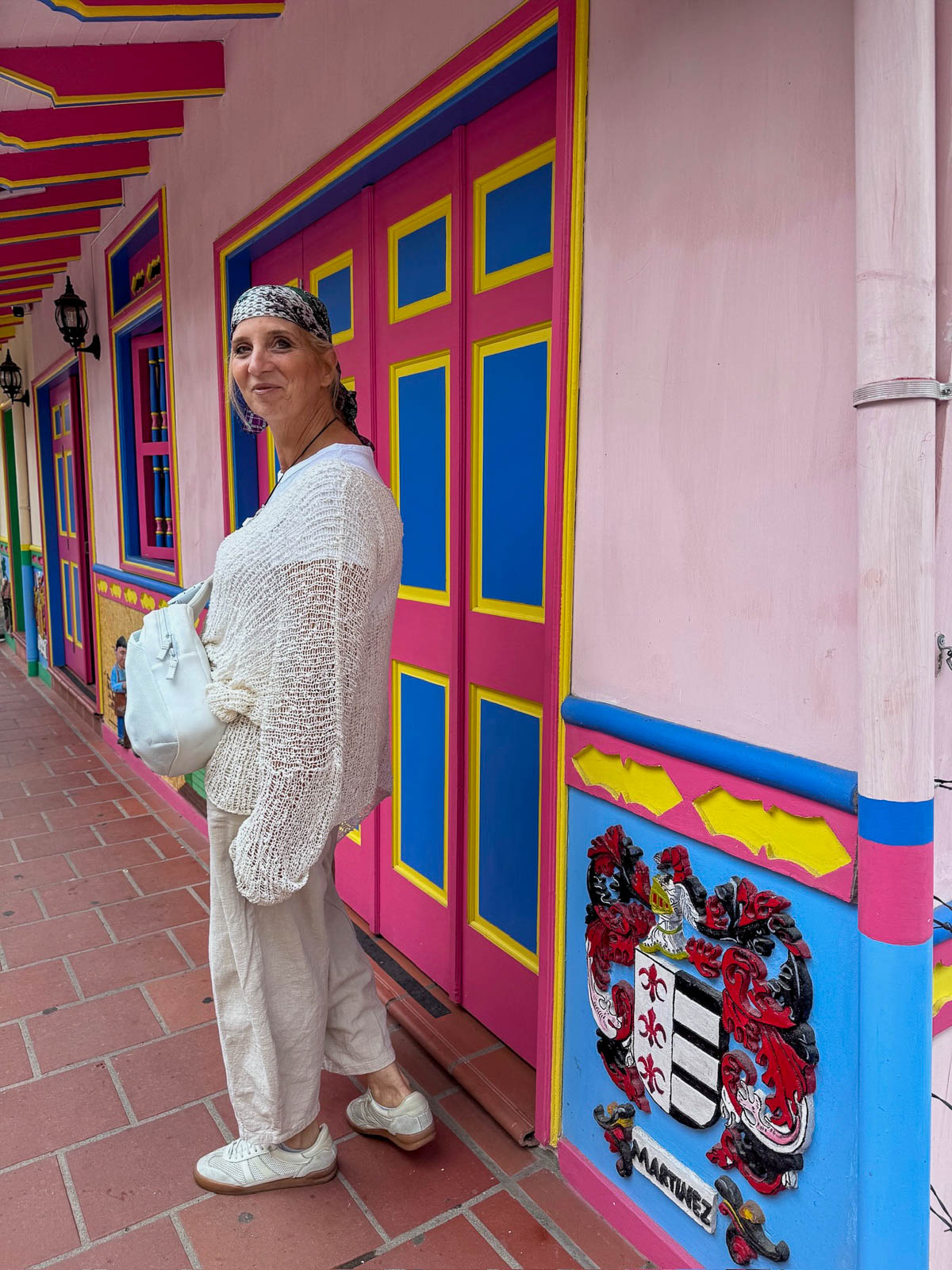 Woman in white next to a pink door with a painted zócalo panel in Guatapé