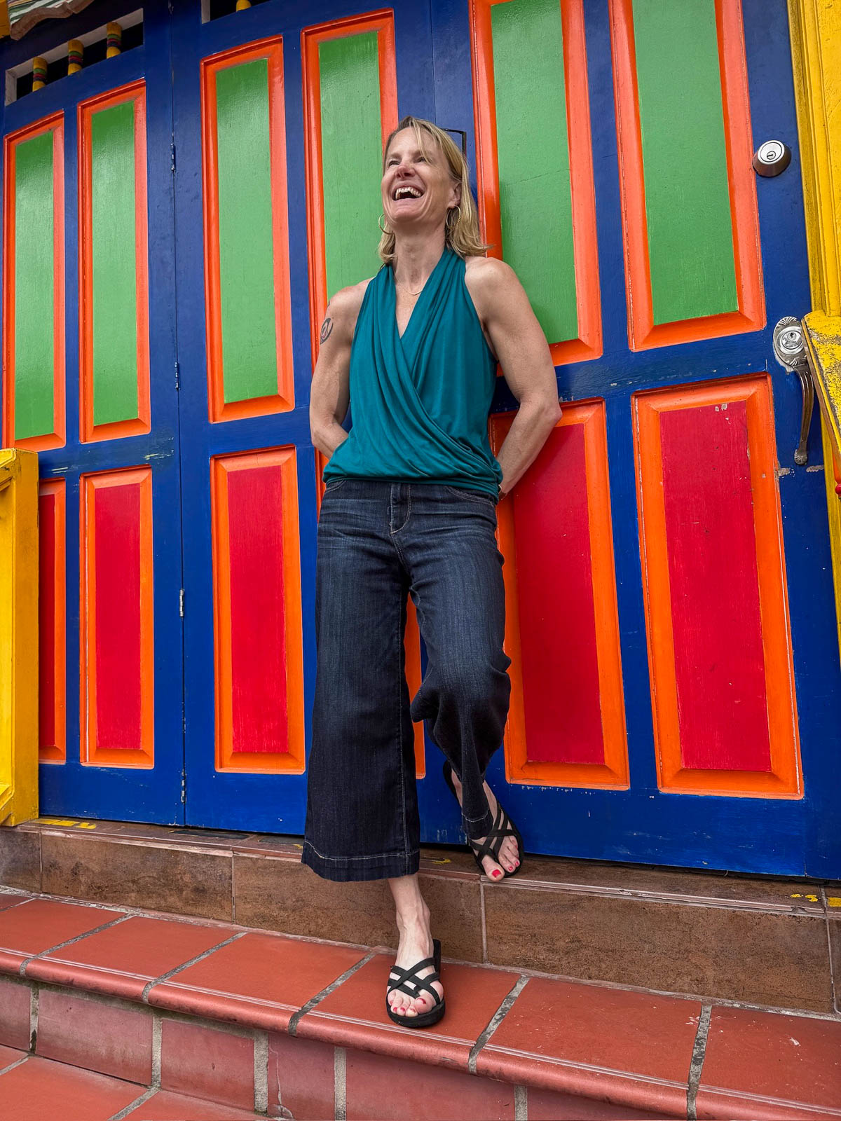 Woman leaning against bright red, green, and blue doors in Guatapé