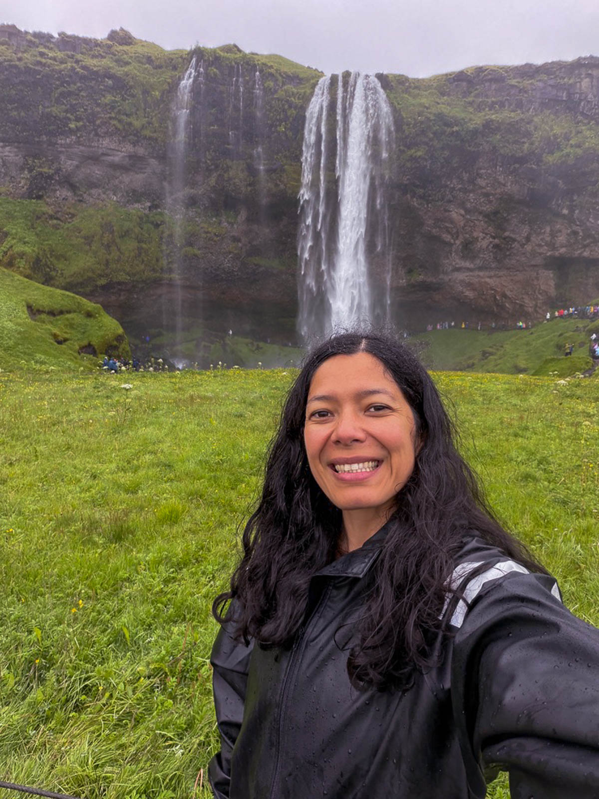 Toni standing in a green field in front of Seljalandsfoss waterfall in Iceland
