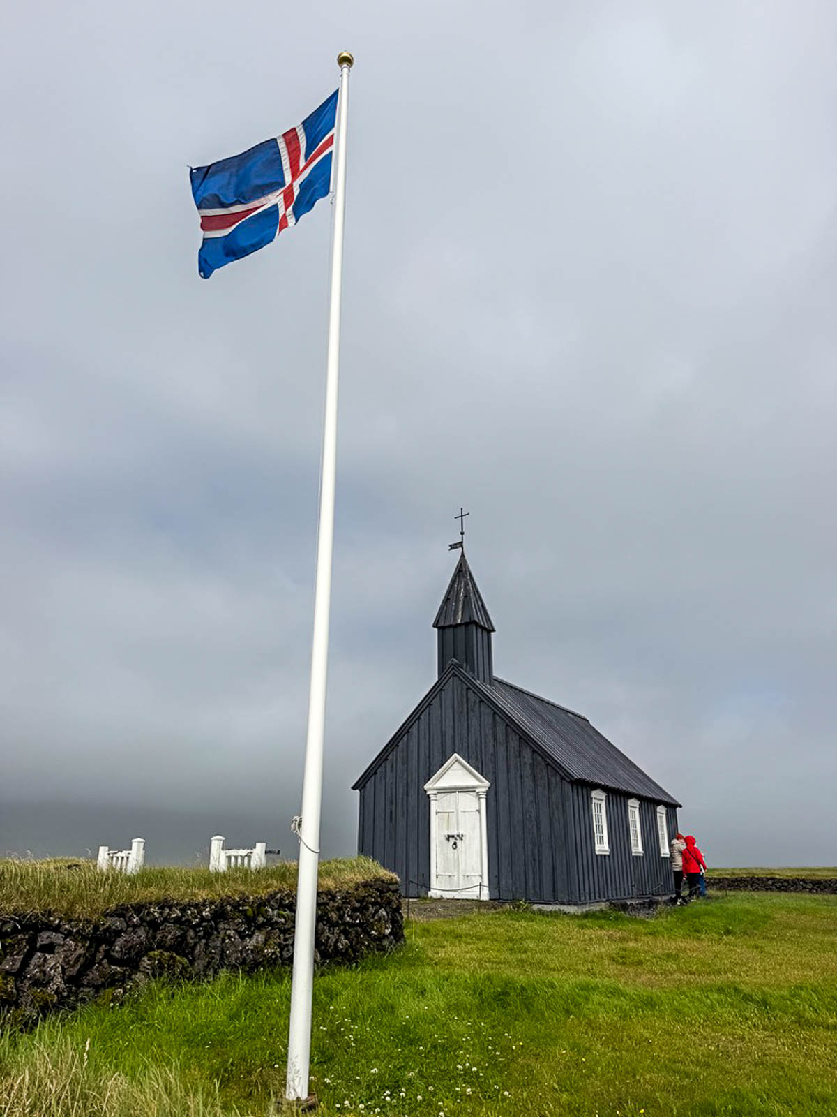 The black church at Búðir with an Icelandic flag flying beside it