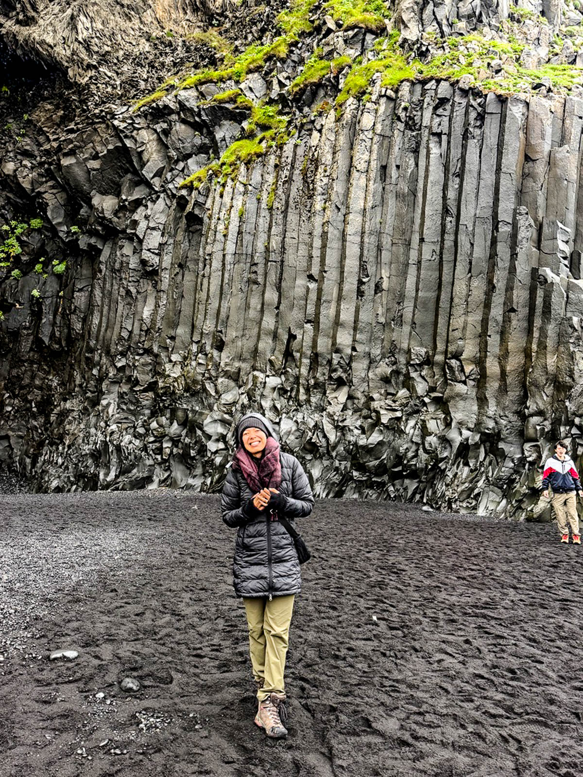 Toni standing on black sand in front of the basalt columns at Reynisfjara beach