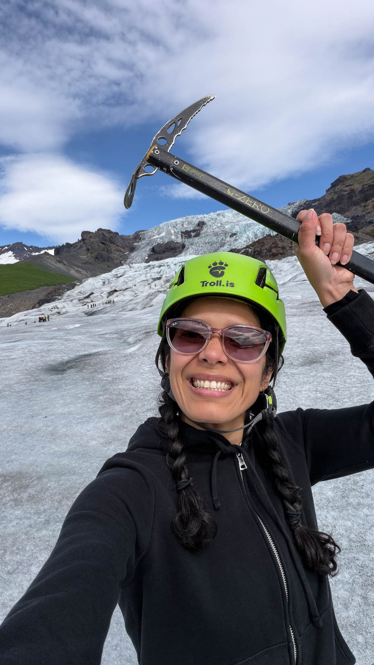Toni in a green helmet raising an ice axe on Sólheimajökull glacier