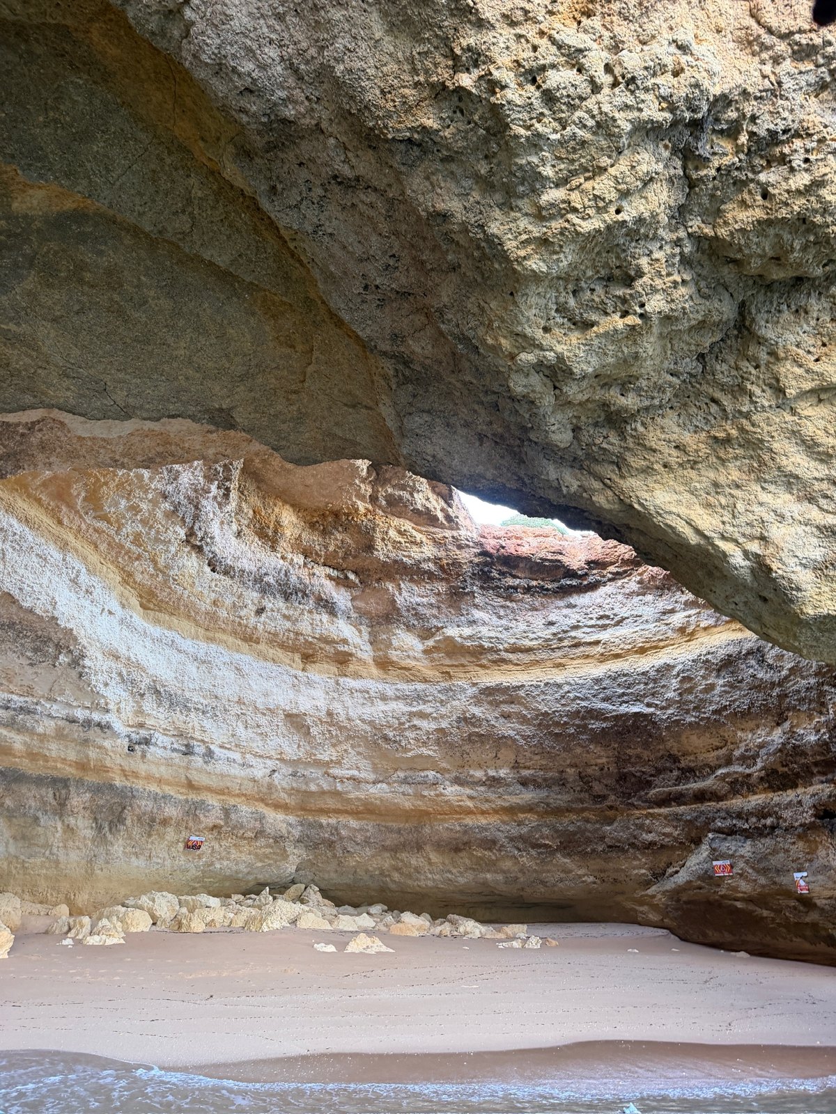 Sandy beach inside the Benagil Cave with layered rock walls