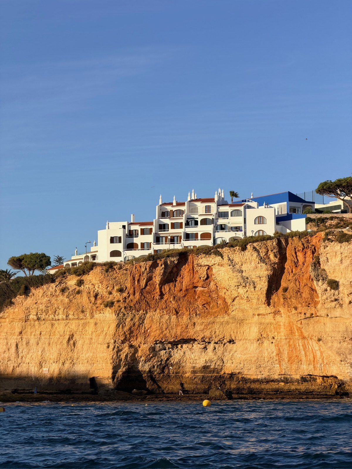 White buildings on top of golden cliffs seen from a boat on the Algarve coast