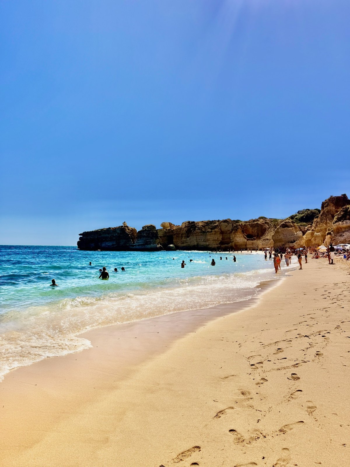 Swimmers and golden cliffs at São Rafael Beach below Kimpton Atlântico Algarve