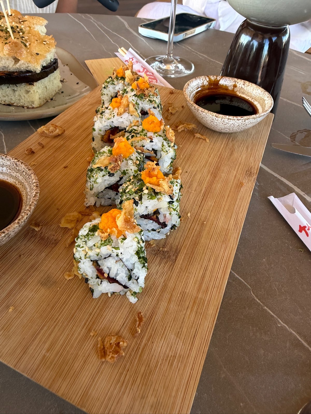 Vegan sushi rolls topped with crispy onions on a wooden board at Zénite Rooftop