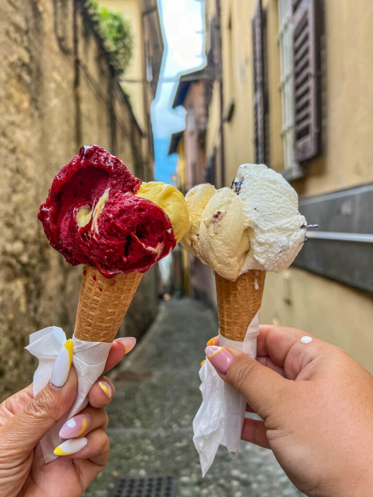 Two hands holding gelato cones in a stone alley in Bellagio.