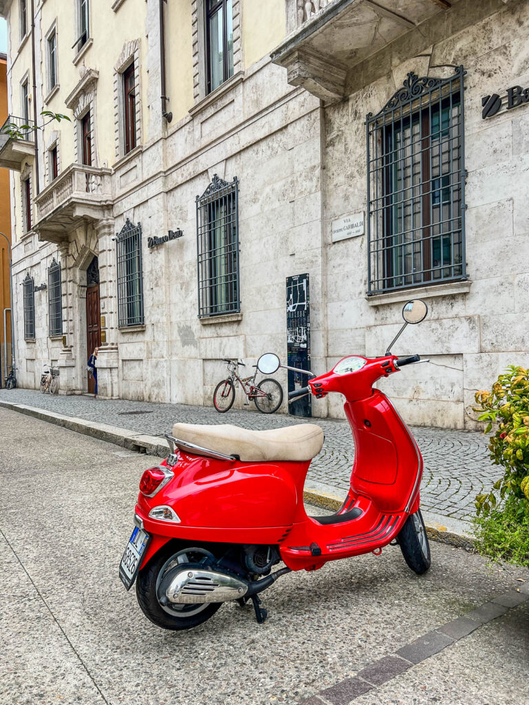 A red Vespa parked on a cobblestone street in Como town.