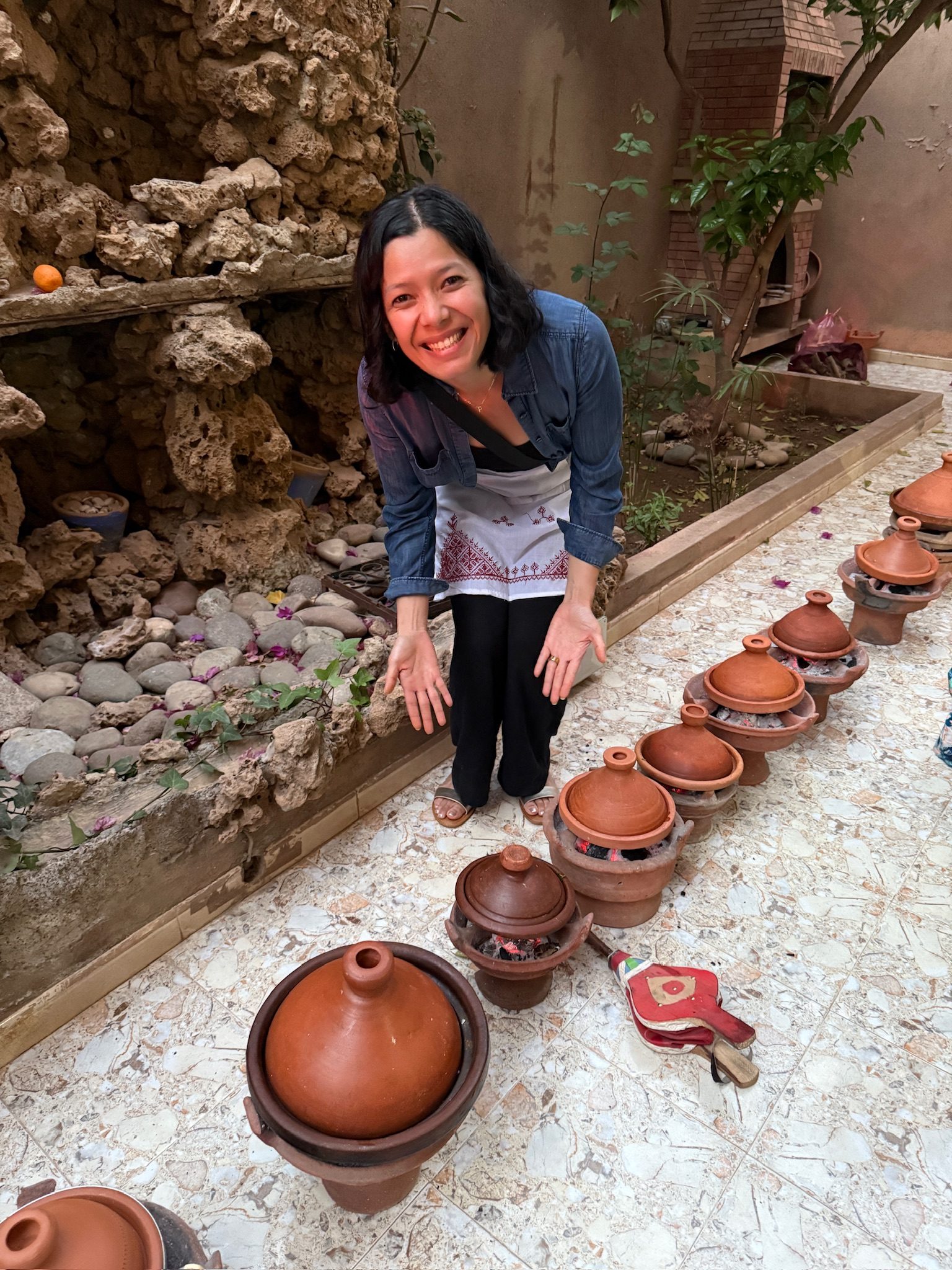 Smiling woman kneeling beside a row of clay tagines in a courtyard