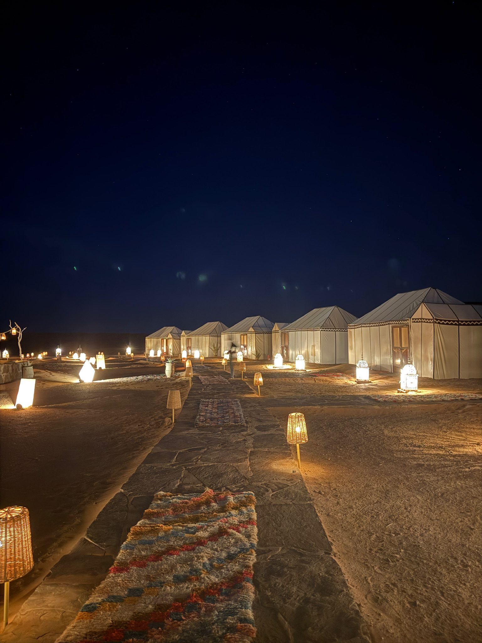 Lantern-lit path between white tents at a desert camp at night