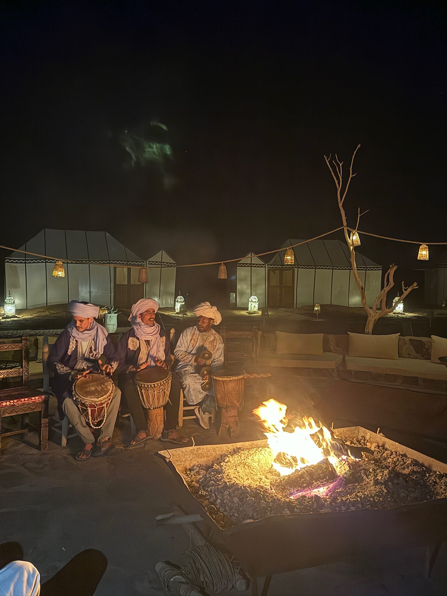 Musicians playing drums beside a fire pit at a Sahara desert camp