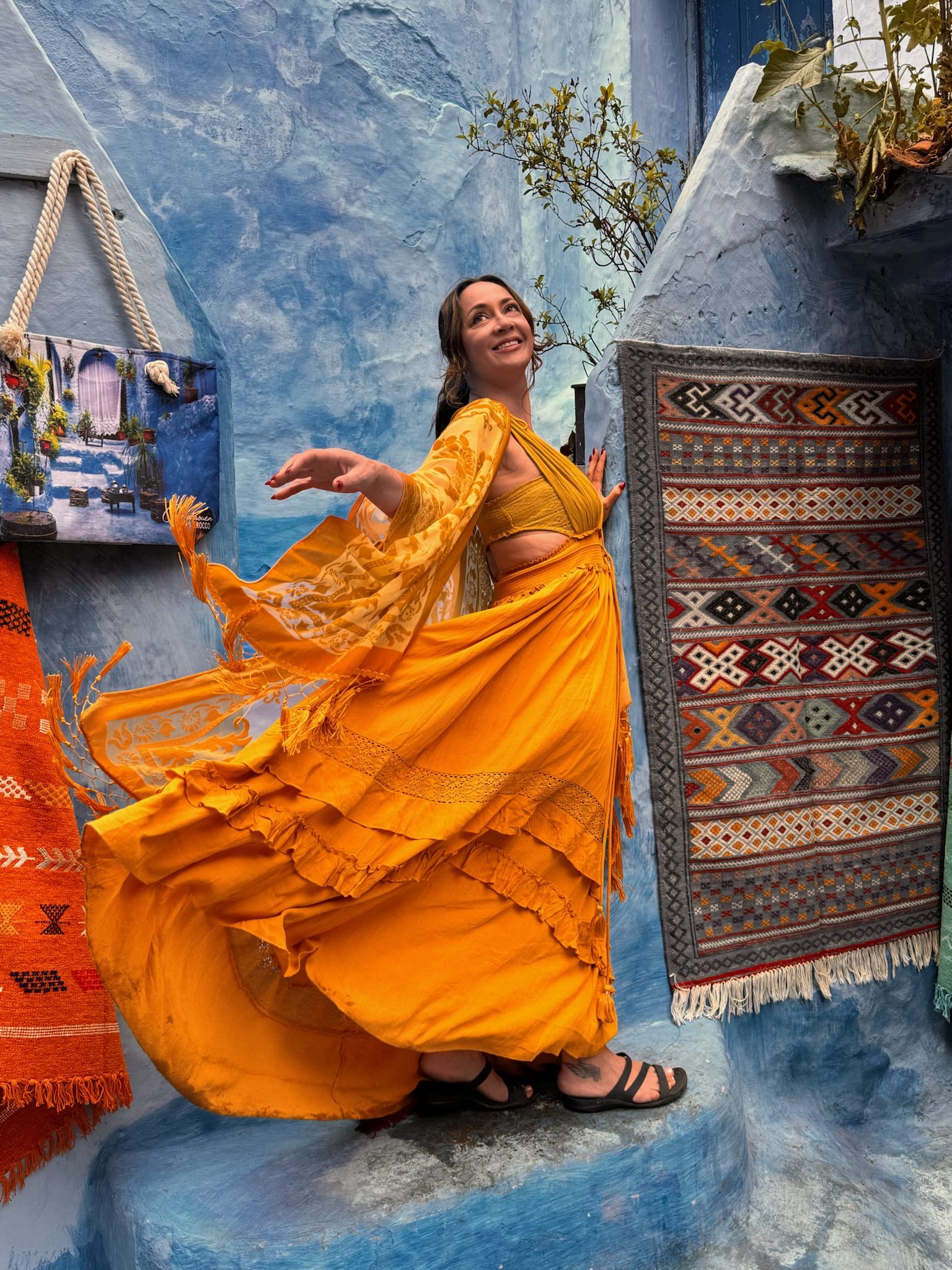 Woman twirling in a flowing yellow dress on a blue street in Chefchaouen