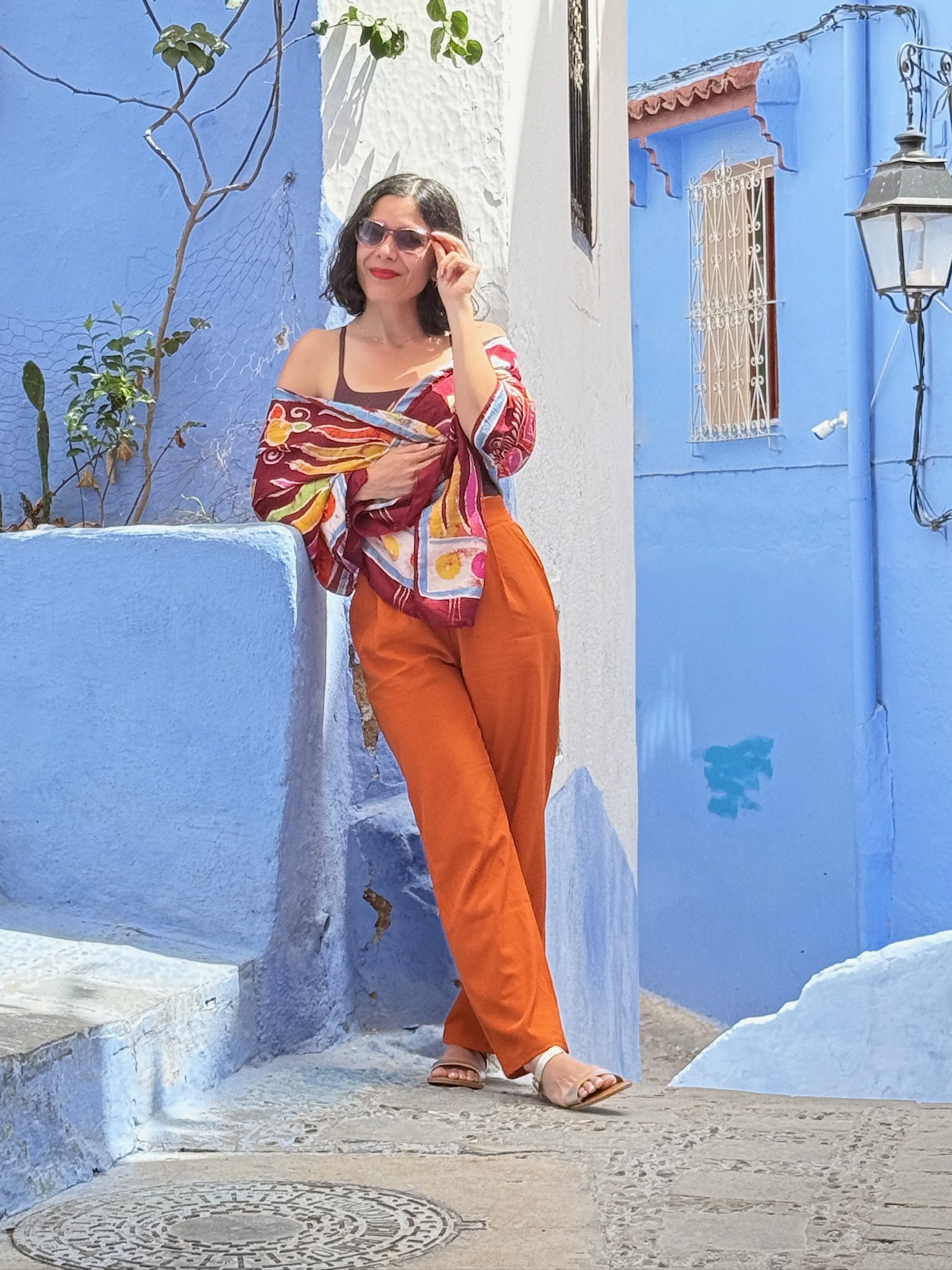 Woman in orange posing on blue-painted steps in Chefchaouen