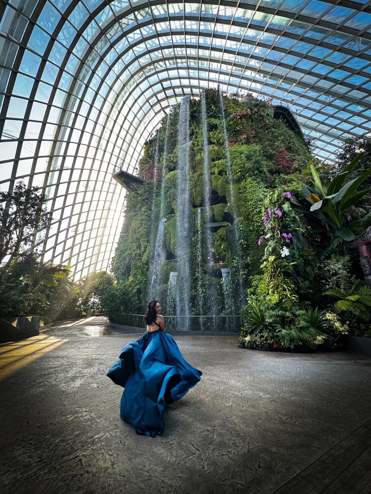 Liz in a blue gown in front of the indoor waterfall at the Cloud Forest, Gardens by the Bay